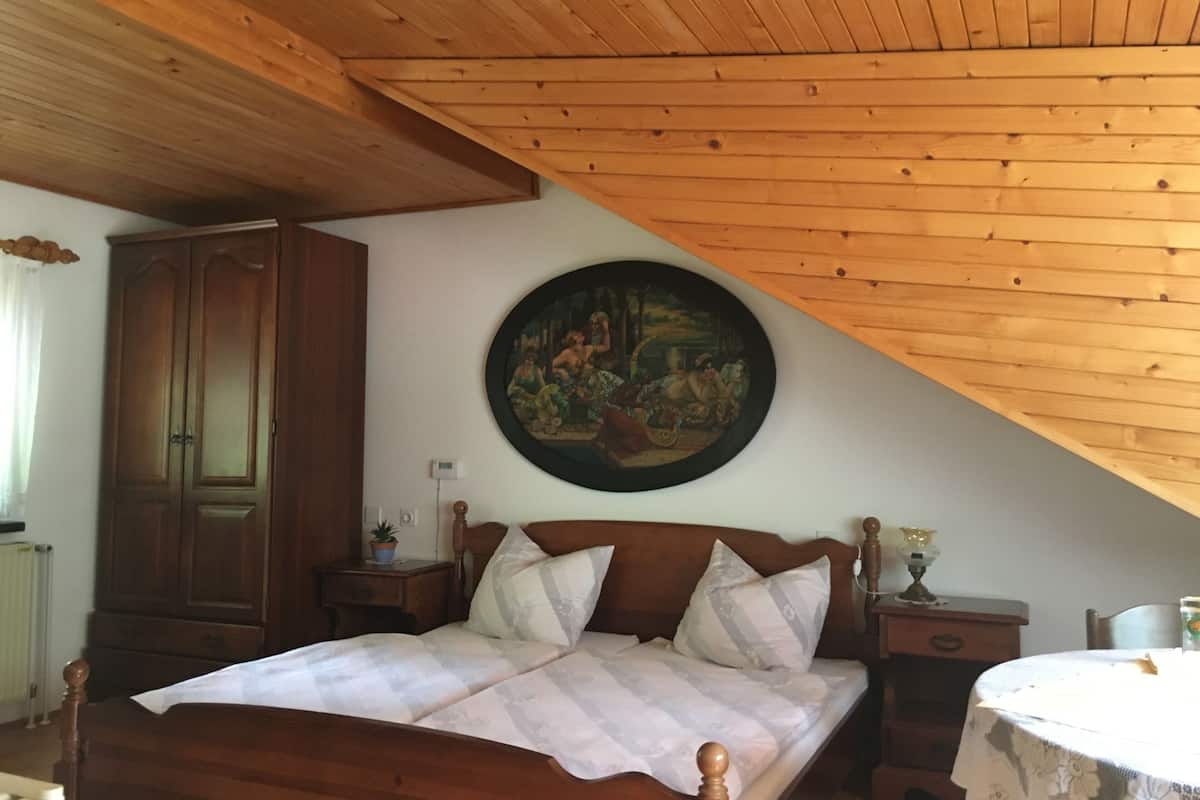 A bedroom with a wooden ceiling, a large bed with a headboard, a nightstand, a dresser, and a painting on the wall.