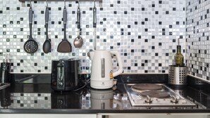 Una cocina con salpicadero de azulejos, cafetera, hervidor y utensilios colgantes.