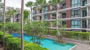 Un hotel moderno con varios balcones, piscina y abundante vegetación.