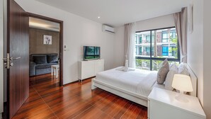 Un dormitorio moderno con una cama grande, un televisor, una mesita de noche blanca y un ventanal con vistas a edificios.