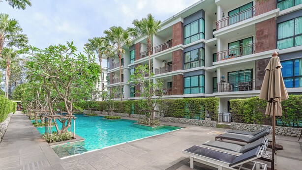Un hotel moderno con zona de piscina, mobiliario exterior y exuberante vegetación.