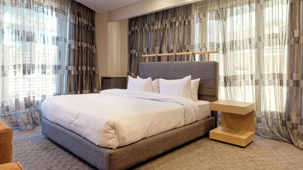 A modern bedroom with a large bed, a wooden bedside table, and sheer curtains. - VESTA - New Cairo Residennce (New Cairo)