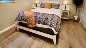 A bedroom with a bed, bedside tables, a mirror, a window with curtains, and a plant.