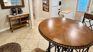 A dining area with a round table and chairs, a coffee station, a washing machine, and a large mirror on the wall.