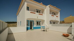 A two-story building with a white facade and blue accents, featuring a balcony and a small patio area with outdoor furniture.