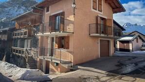 A two-story chalet with wooden balconies and a stone staircase. - Chalet with panoramic view · Modern comfort · Quick access to 3 Vallées (Les Belleville)