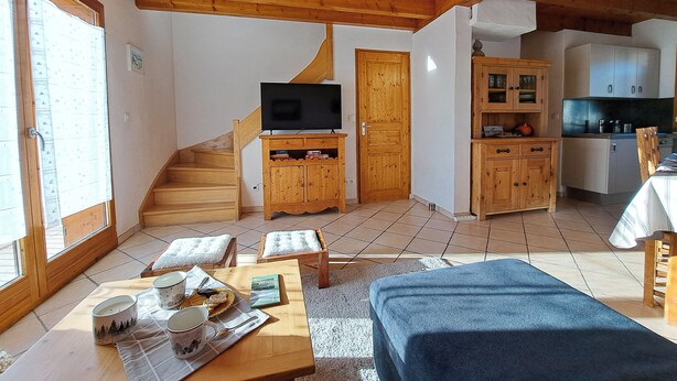 A cozy room with a wooden ceiling, a TV on a wooden cabinet, a staircase, and a kitchen area. - Chalet with panoramic view · Modern comfort · Quick access to 3 Vallées (Les Belleville)