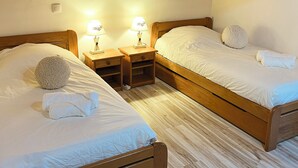 A room with two wooden beds, each with a pillow and a lamp. There are wooden nightstands and a small shelf between the beds. The room has wooden beams on the ceiling. - Chalet with panoramic view · Modern comfort · Quick access to 3 Vallées (Les Belleville)