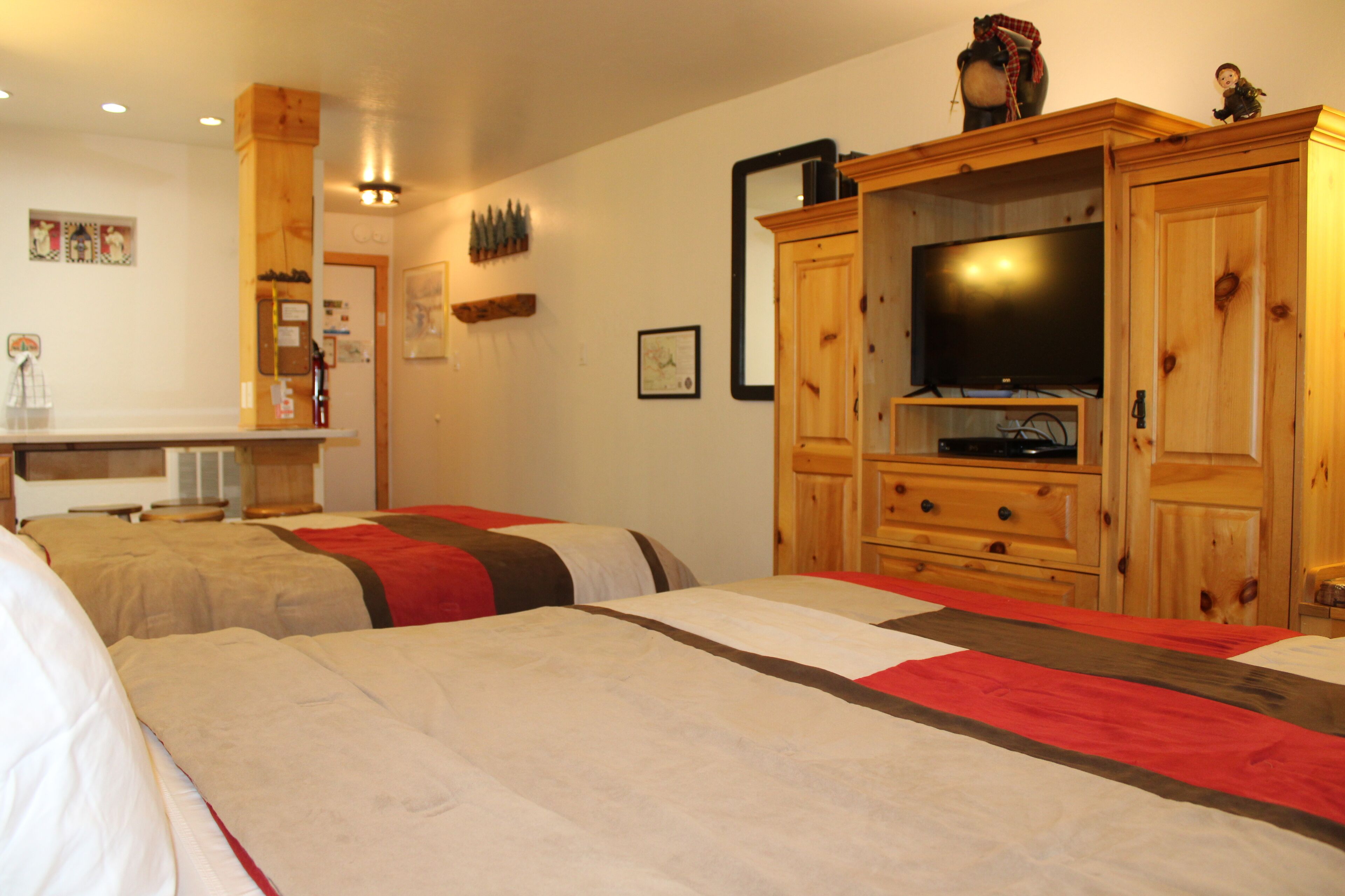 Una camera d'albergo con due letti, un armadio in legno con un televisore e un tavolino con una sedia.