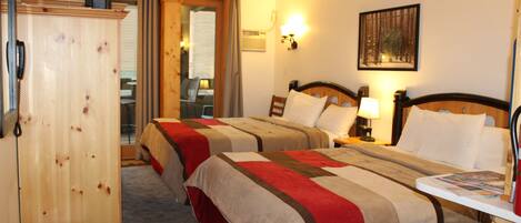 A hotel room with two beds, a wooden wardrobe, a desk with a chair, and a painting on the wall.