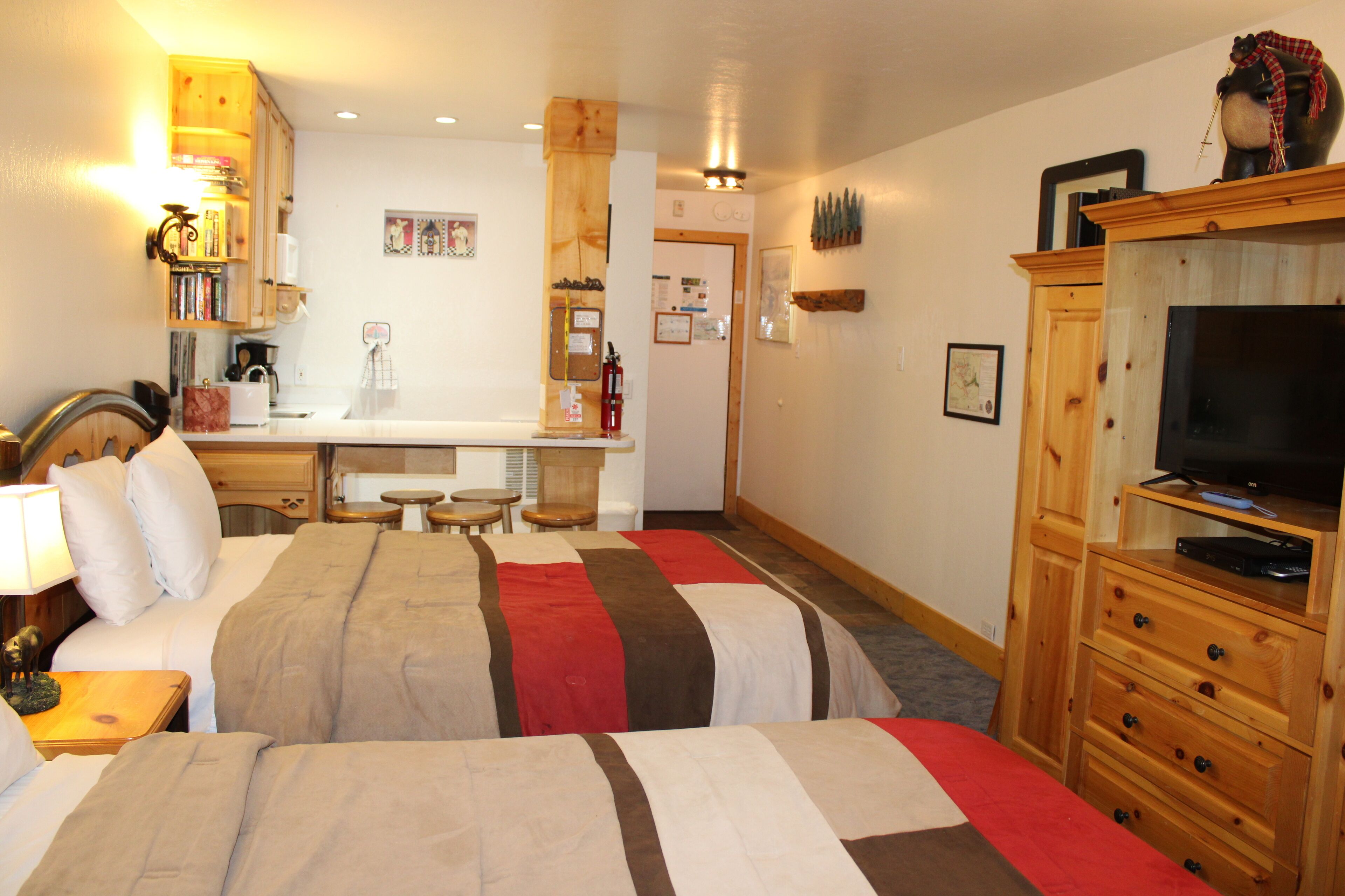 Une chambre d’hôtel avec deux lits, une commode en bois, une télévision et un coin cuisine.
