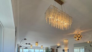 A spacious dining area with a long wooden table and blue chairs, a chandelier, and a city view through large windows. - VESTA - Mohandessin (Giza)