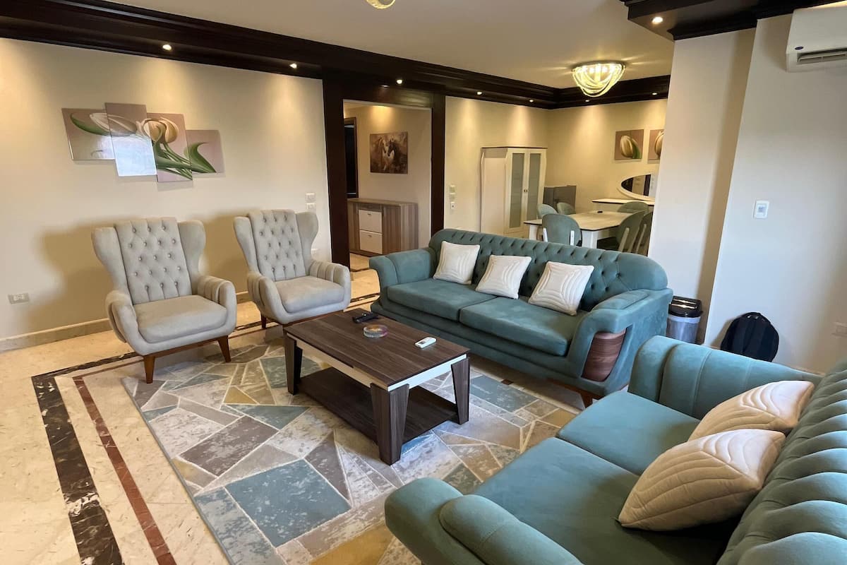 A living room with a green sofa, two armchairs, a coffee table, and a patterned rug.