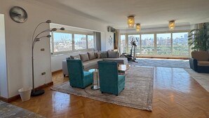 A spacious living room with a large sofa, teal chairs, and a herringbone wooden floor. - VESTA - Mohandessin (Giza)