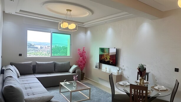 Een moderne woonkamer met een bank, salontafel, eettafel, stoelen en een televisie.