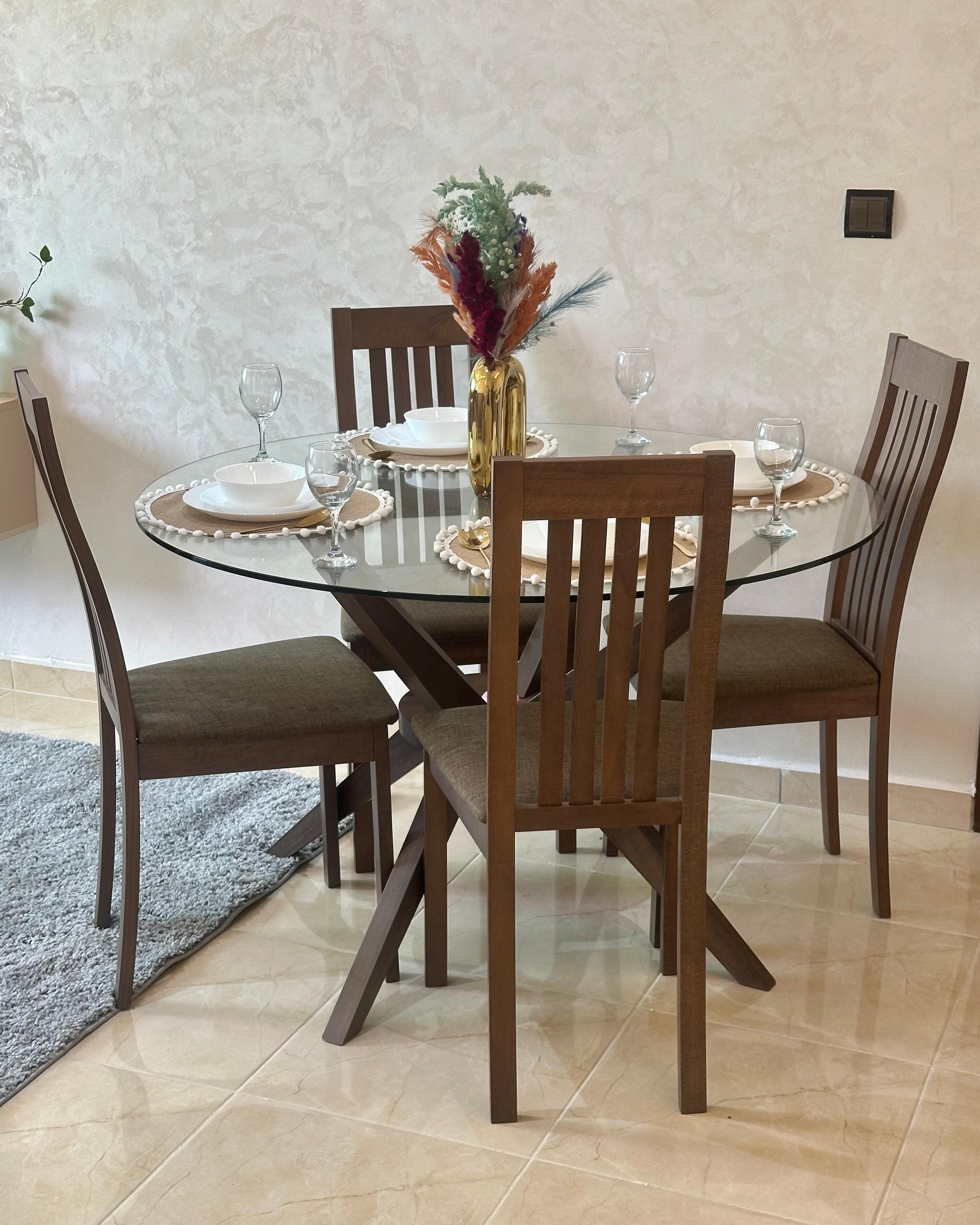 A dining table with four chairs, a vase with flowers, and a wall-mounted light fixture.
