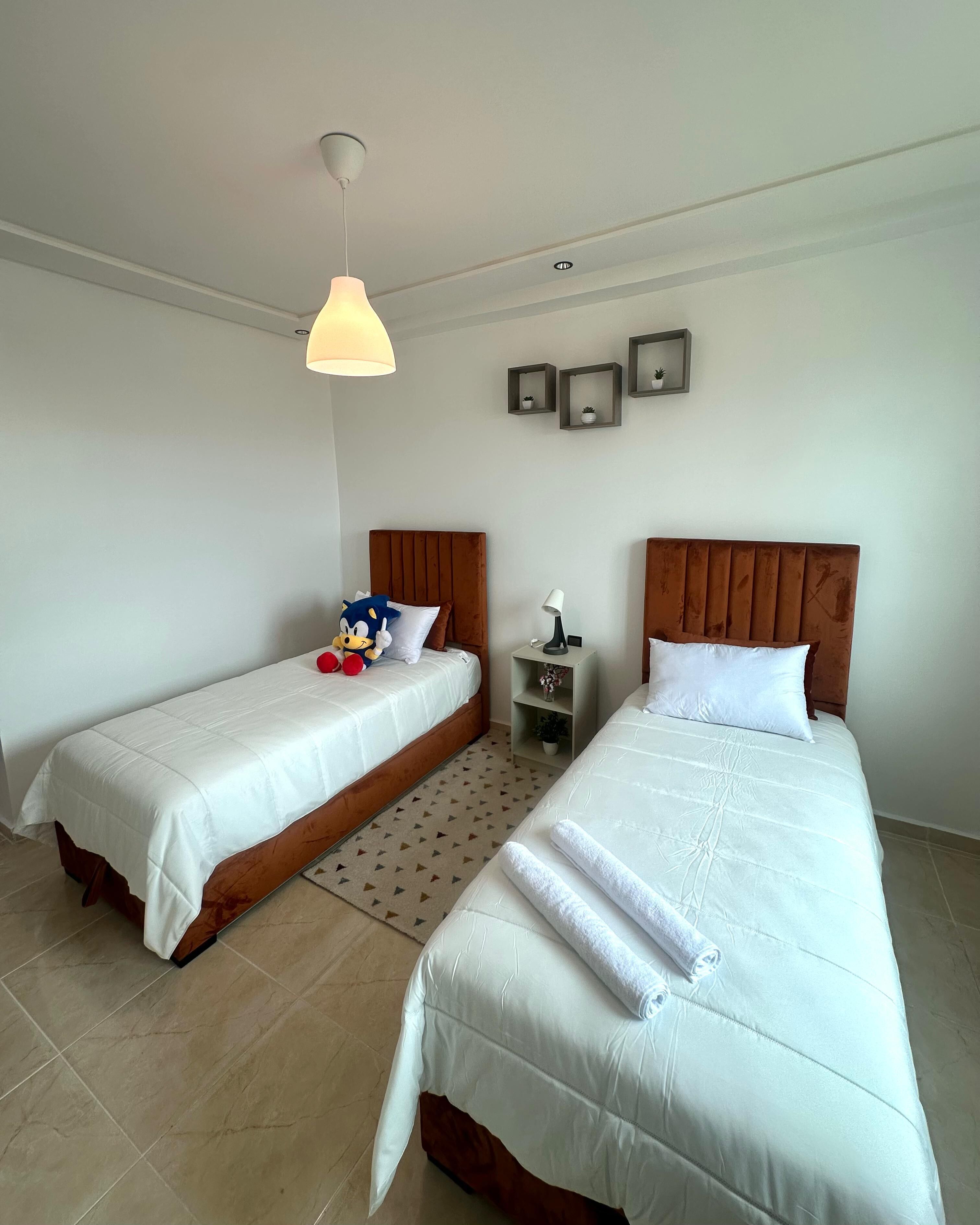 Une chambre d’hôtel avec deux lits, une table de chevet, une lampe et un luminaire au plafond.