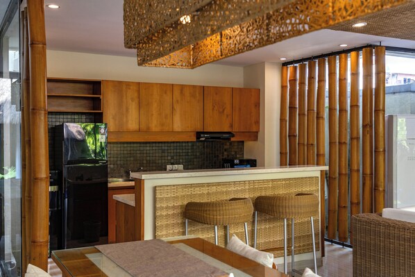 A modern kitchen with wooden cabinets, a refrigerator, and a bar area with two stools.