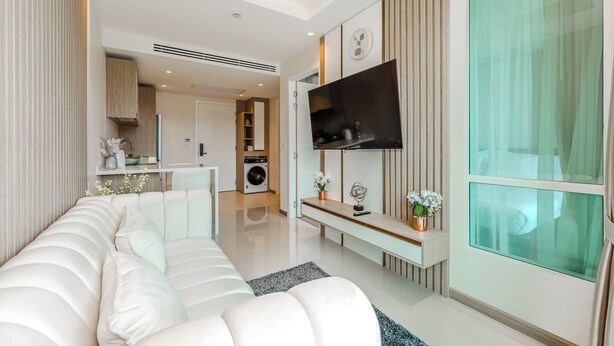 Een moderne woonkamer met een bank, een aan de muur bevestigde televisie en een keuken in de achtergrond.