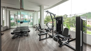 Een moderne fitnessruimte met cardioapparatuur, krachttrainingapparatuur en grote ramen met uitzicht op groen en gebouwen.