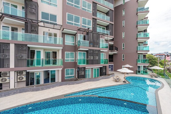 A multi-story residential building with balconies, a swimming pool, and outdoor seating. - 1BR Pool Gym Game Room C220 (Wichit)