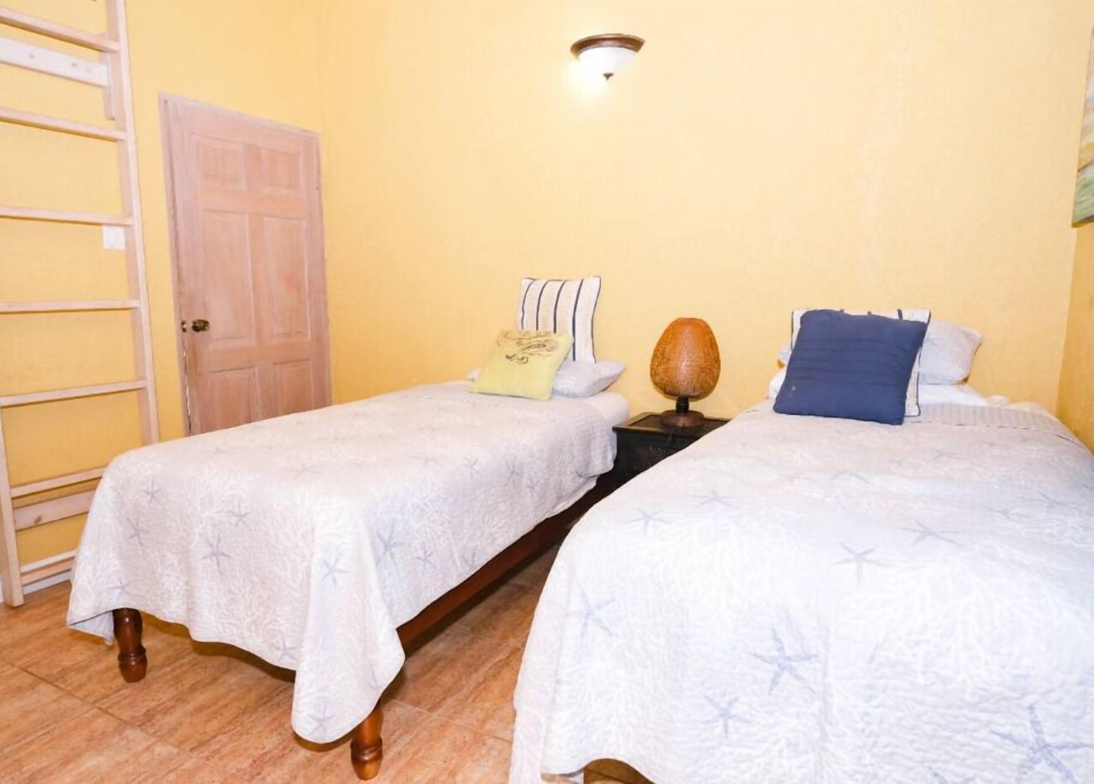 A room with two beds, a wooden door, a wall-mounted light fixture, and a wooden ladder.