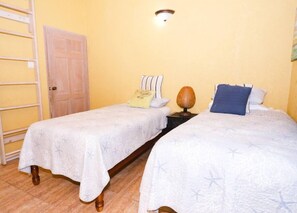 A room with two beds, a wooden door, a wall-mounted light fixture, and a wooden ladder.