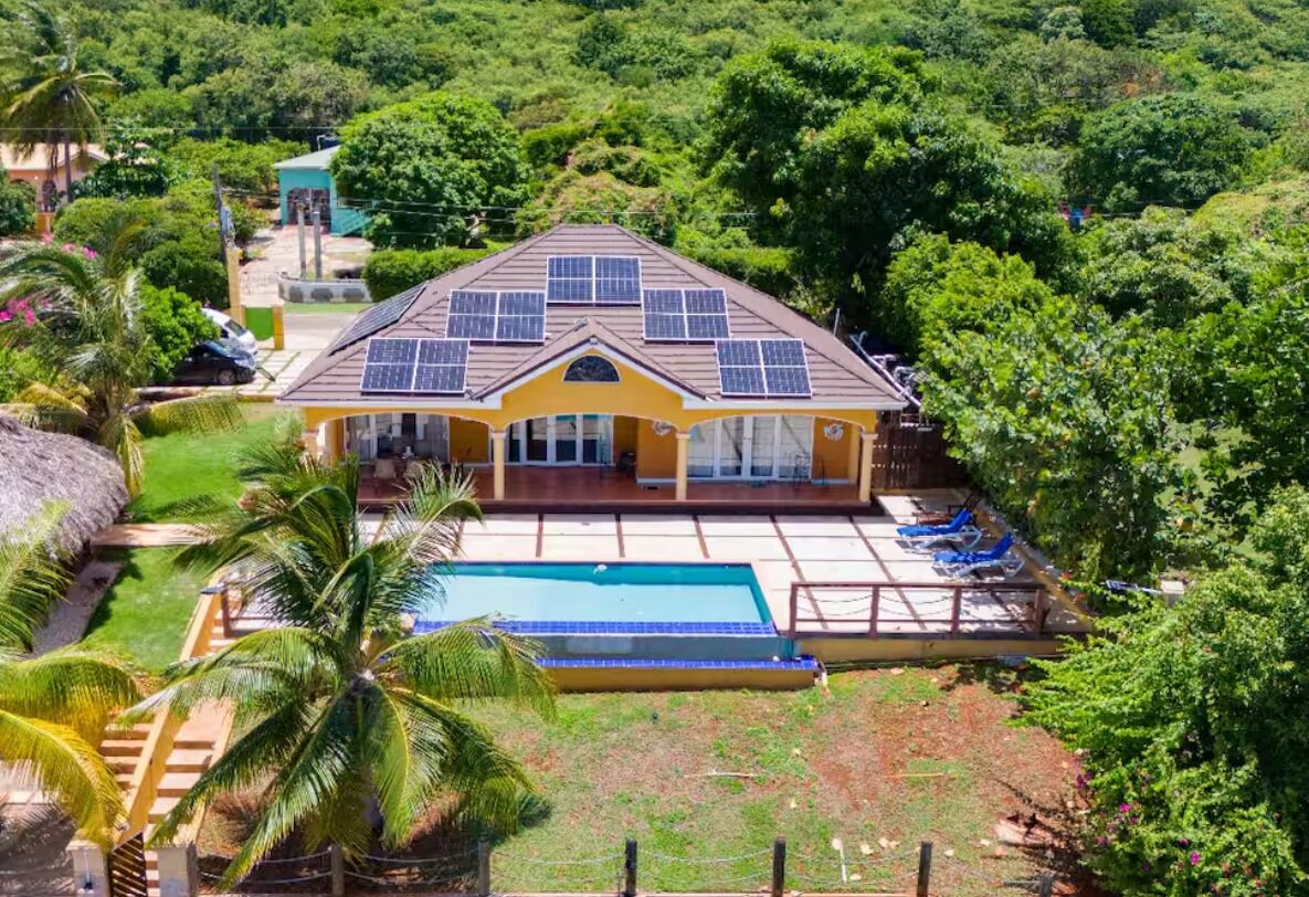 A house with a swimming pool, surrounded by lush greenery and palm trees.