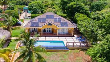 A house with a swimming pool, surrounded by lush greenery and palm trees.