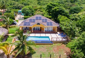 A house with a swimming pool, surrounded by lush greenery and palm trees.