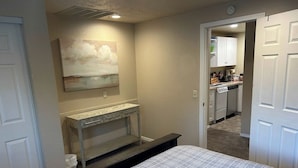A bedroom with a bed, a nightstand, a painting on the wall, and a view into the kitchen. - Walk to Downtown CDA | Sleeps 8 | Arcade + Pets (Coeur d'Alene)