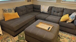 A modern living room with a sectional sofa, a small ottoman, and a tray table. - Walk to Downtown CDA | Sleeps 8 | Arcade + Pets (Coeur d'Alene)