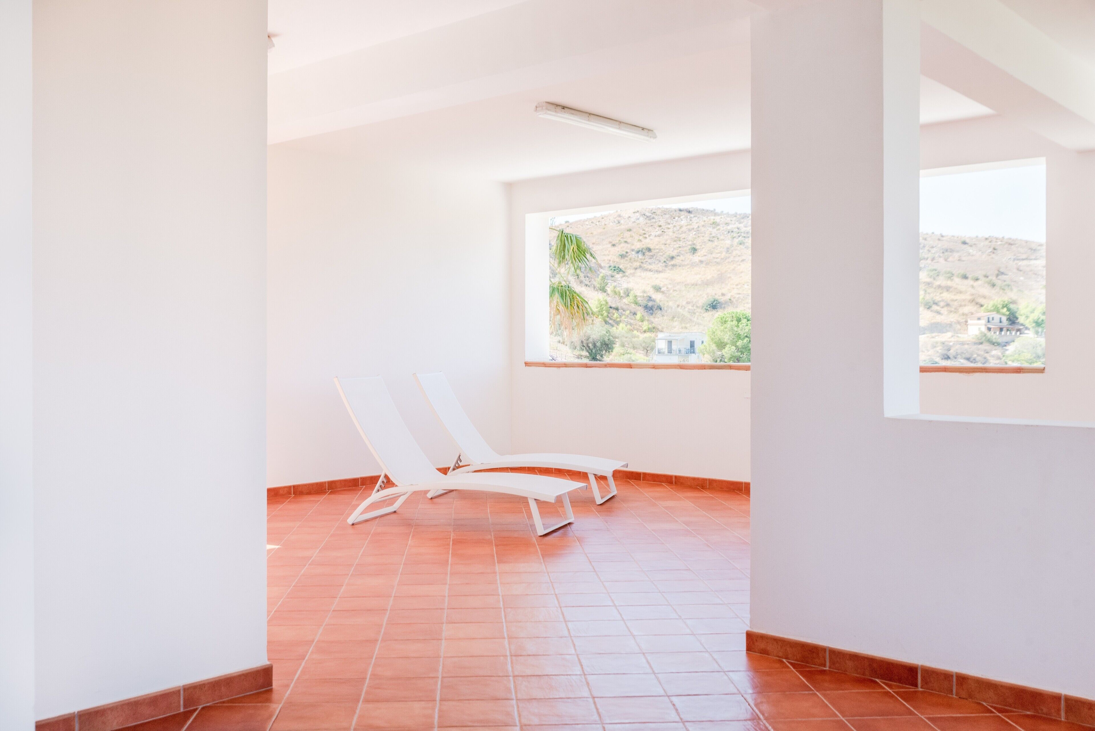 Una habitación con piso de baldosas, techo blanco y ventana con vista a un paisaje montañoso.