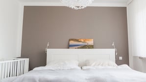 Een slaapkamer met een wit hoofdeinde, een schilderij van een landschap en een witte radiator.