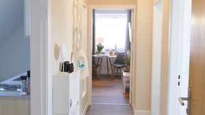 A narrow hallway with a kitchen area on the left, a dining area with a table and chairs in the center, and a door on the right.