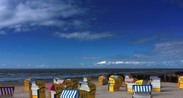 A beach with yellow beach chairs and umbrellas, a clear blue sky, and the ocean in the background.
