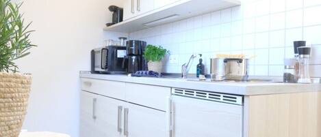 Una cocina moderna con armarios blancos, una cafetera, una planta y un lavamanos.