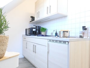 A modern kitchen with white cabinetry, a coffee maker, a plant, and a sink.