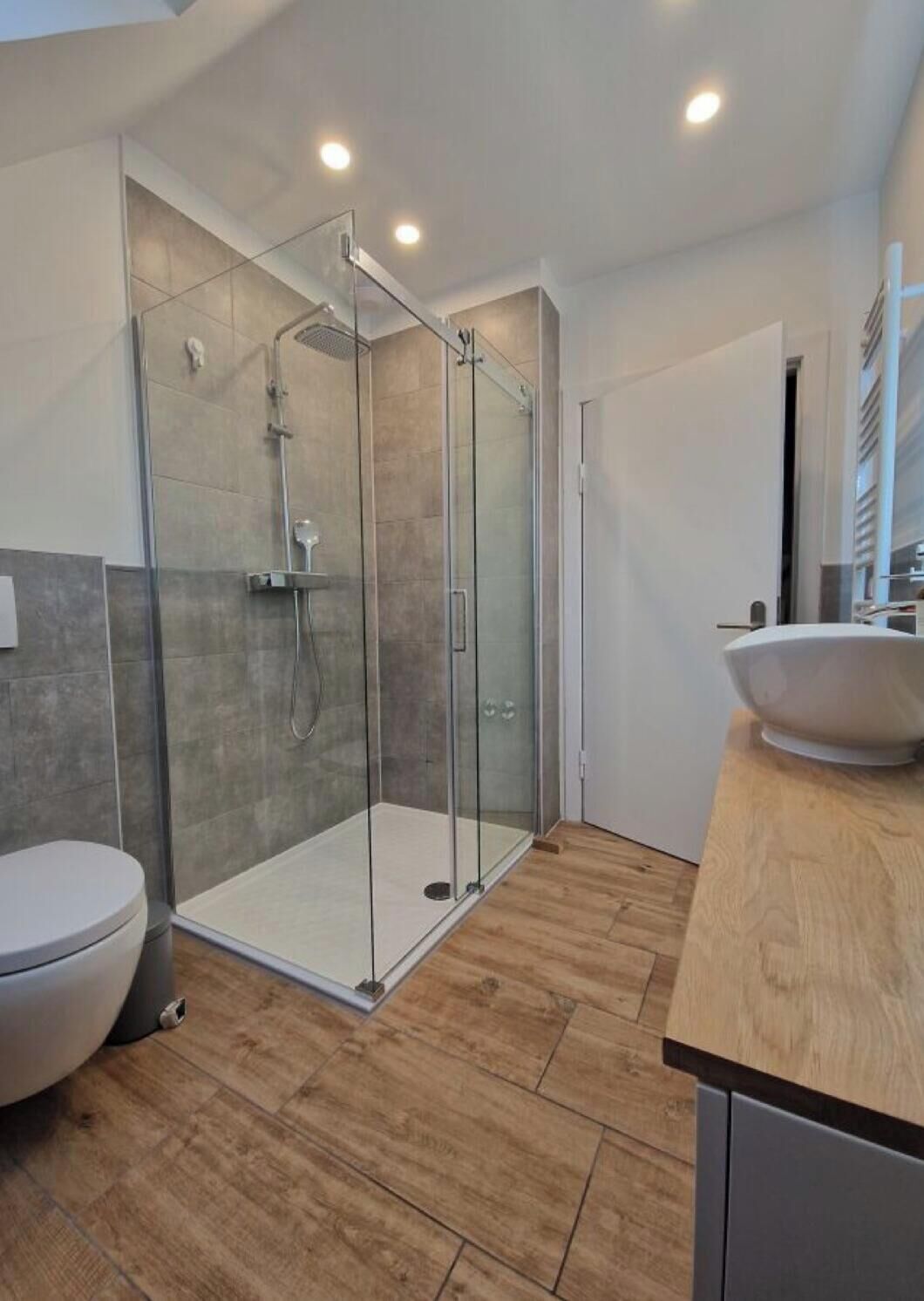 Ein modernes Badezimmer mit einer Duschkabine, einer Toilette und einem Holzbadezimmer-Möbel mit Waschbecken.
