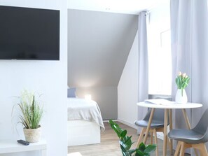 Une chambre d’hôtel moderne, équipée d’un lit, d’une petite table avec des chaises, d’une plante en pot et d’un téléviseur fixé au mur.