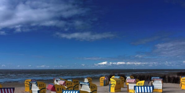Une plage avec des chaises longues et des parasols jaunes, un ciel bleu clair et l’océan en arrière-plan.