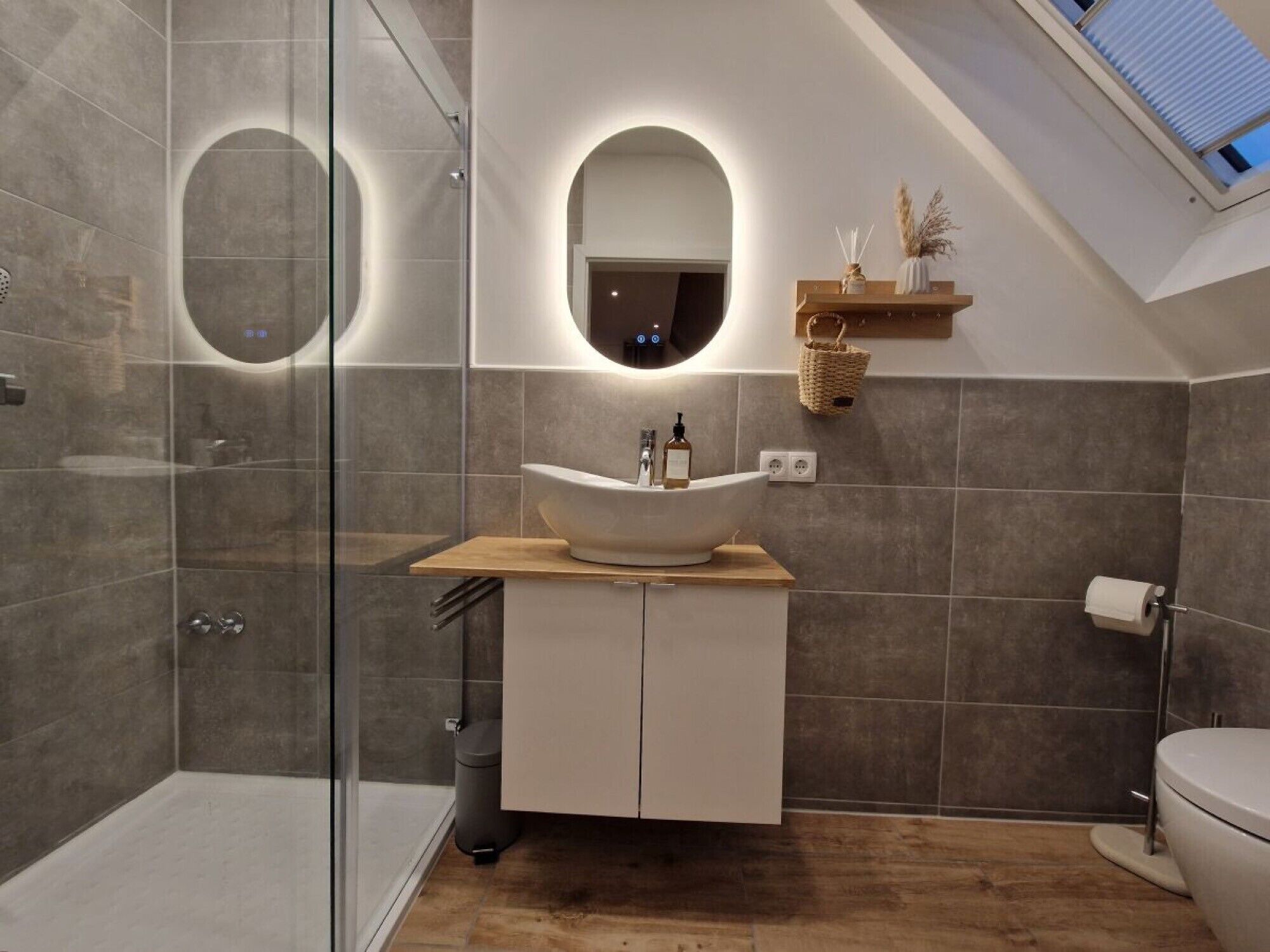 A modern bathroom with a glass-enclosed shower, a vessel sink, and a skylight.