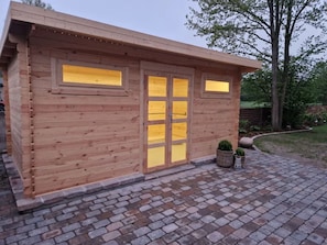 A wooden cabin with a brick-paved entrance, large windows, and a small garden area. - Holiday Apartments Haus Bärbel Duhnen Apartment '4' (Cuxhaven)