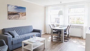 Un salon comprenant un canapé, une table basse, une table à manger avec des chaises et une fenêtre avec des rideaux.