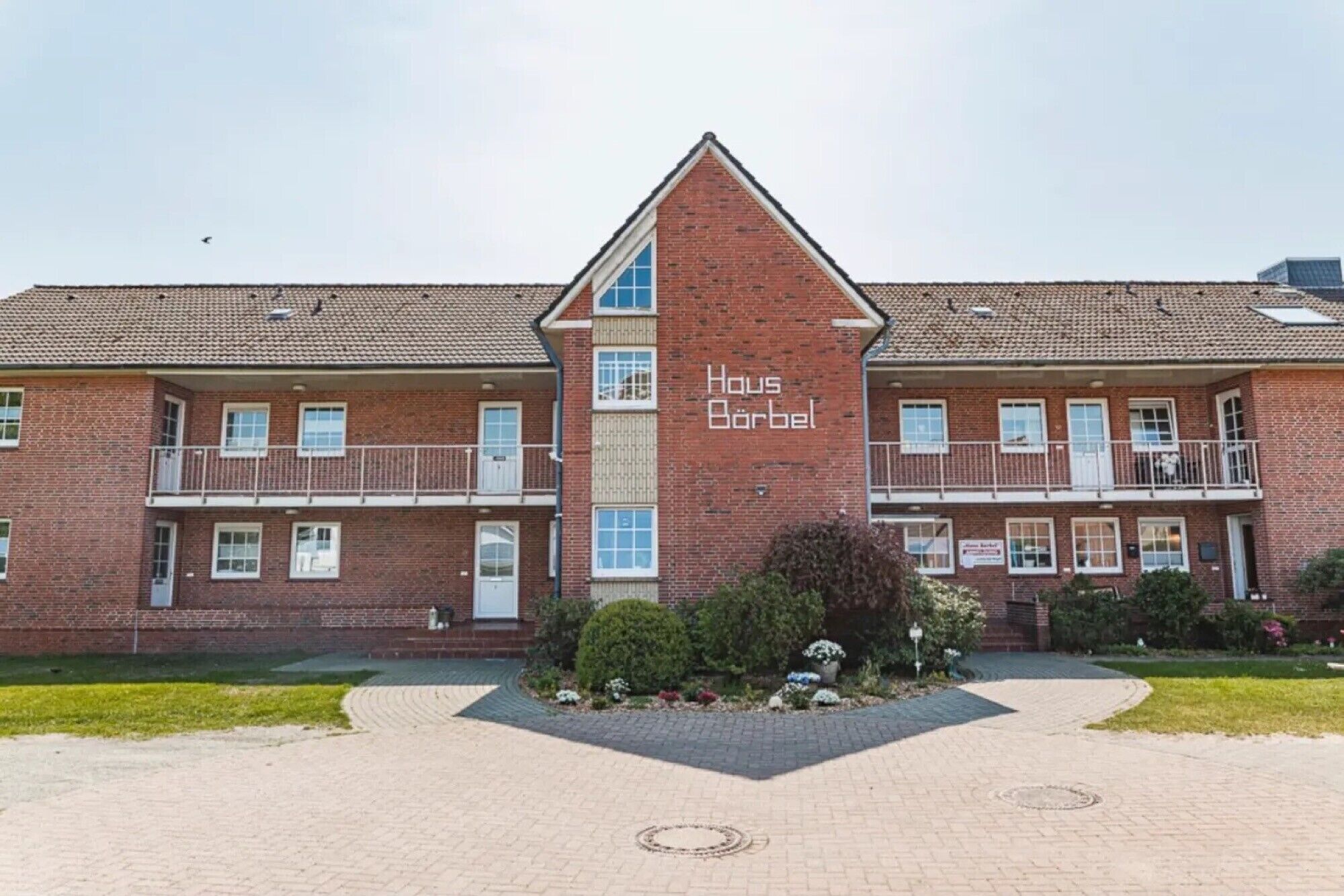 A two-story brick building with a central entrance and a sign reading 'Haus Bärbel.'