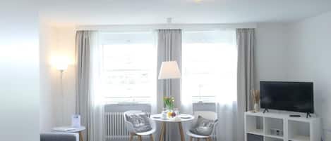 A modern hotel room with a bed, a TV, a dining area with chairs and a table, and a sofa.