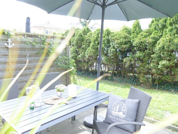 An outdoor patio with a table and chairs, a potted plant, and a large umbrella.