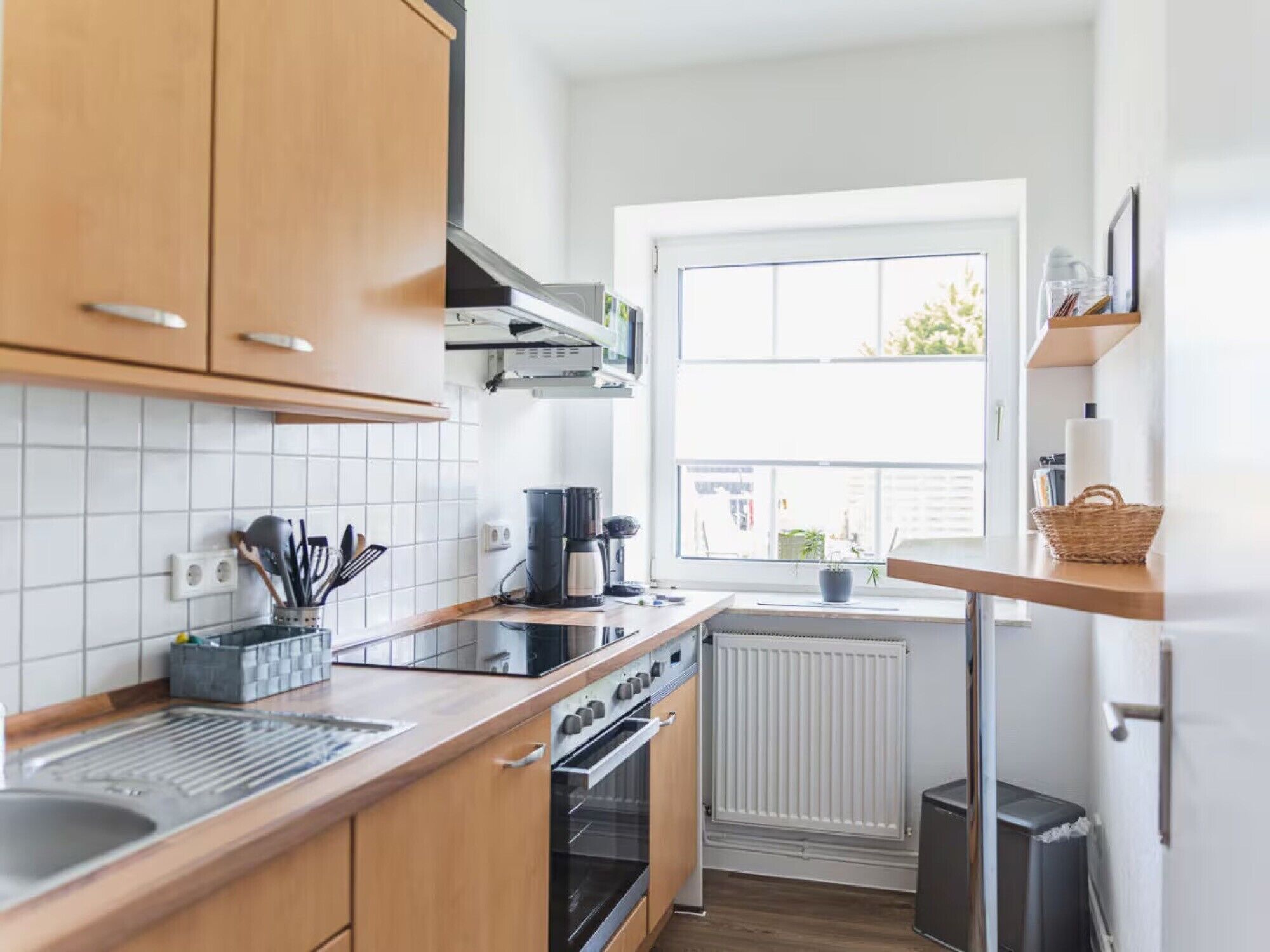 Eine moderne Küche mit Holzausstattung, einem eingebauten Backofen, einer Kaffeemaschine und einem Fenster mit Außenblick.