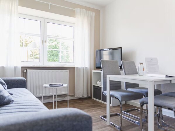 Une pièce moderne comprenant un canapé, une table à manger avec des chaises, un téléviseur et une fenêtre avec des rideaux.