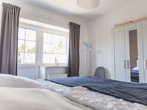 Une chambre à coucher comprenant un lit, un bureau, une chaise, une armoire et une fenêtre avec des rideaux.
